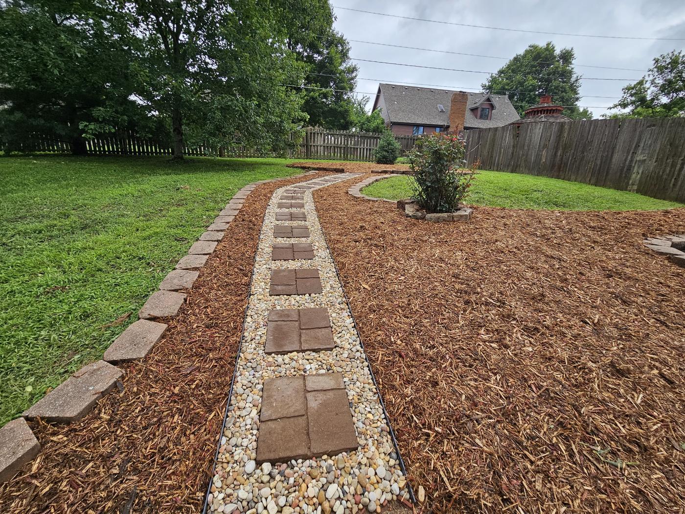 A curving paver path set into river pebble with block edging and mulch beds either side