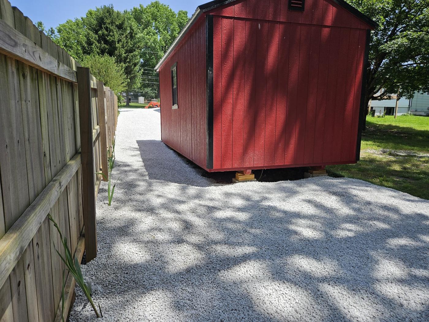 A red shed set on a freshly laid white gravel pad beside a new timber privacy fence